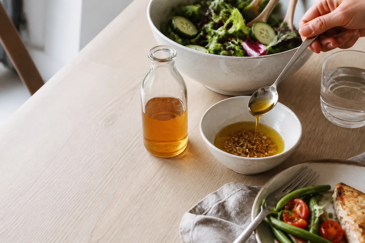 Äppelcidervinäger bredvid en sallad och en liten skål med vinägrett